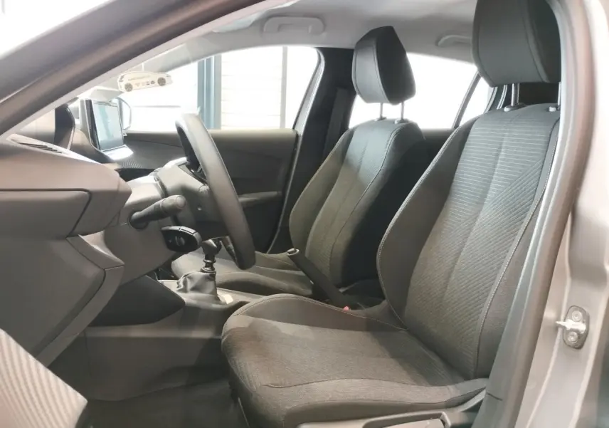 Vue intérieure côté gauche de la Peugeot 208 gris clair, montrant sièges avant en tissu et volant avec boîte manuelle.