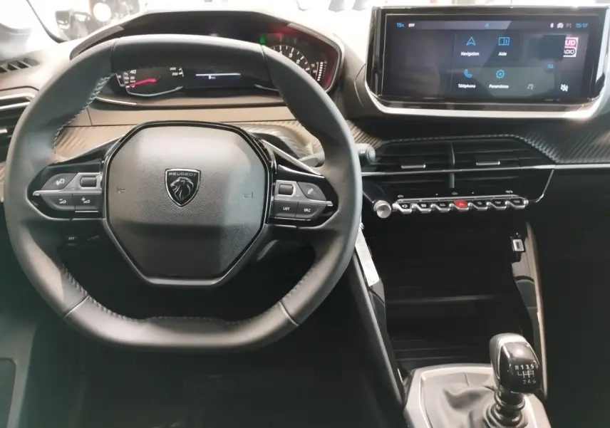 Vue intérieure centrée sur le volant cuir et la console avec écran tactile 10'' de la Peugeot 208 1.2i 12V gris clair, boîte manuelle.