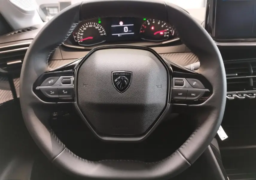 Vue rapprochée du volant noir cuir de la Peugeot 208 2025 avec commandes multimédia et combiné digital en arrière-plan.