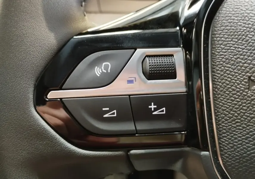 Gros plan sur les commandes noires et argentées du volant de la Peugeot 208 gris clair, version 2025.