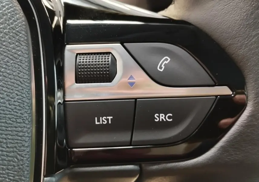 Gros plan sur les commandes multimédia noires et argentées du volant côté gauche d'une Peugeot 208 gris clair.