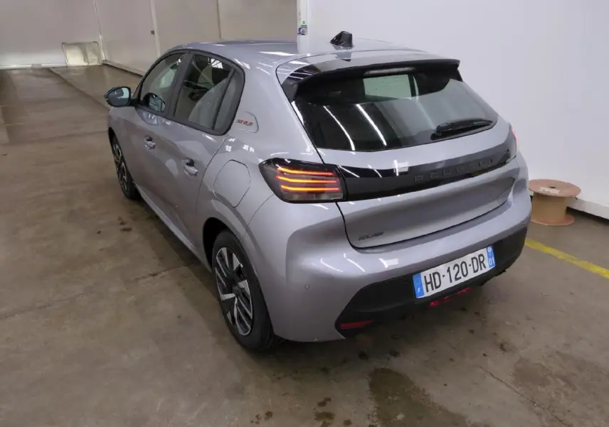 Vue 3/4 arrière droite d'une Peugeot 208 gris clair avec bandeau noir brillant entre feux et badge Style sur custode.