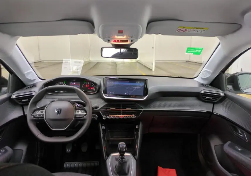 Vue intérieure avant du Peugeot 208 gris clair 2025 avec tableau de bord carbone et écran tactile 10 pouces.
