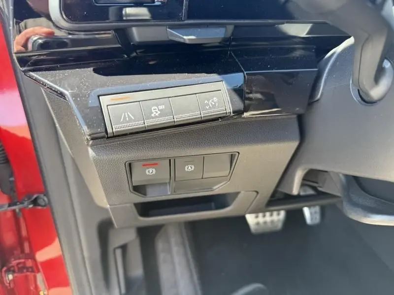Détail intérieur côté gauche du tableau de bord du Renault Austral rouge flamme 2023 avec boutons d’assistance et frein à main électronique.