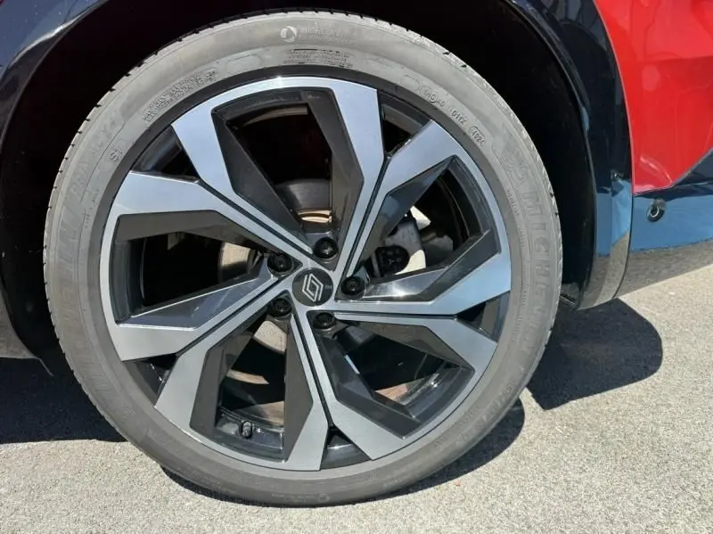 Gros plan sur la jante avant droite du Renault Austral rouge flamme, avec un design moderne bicolore noir et argent.