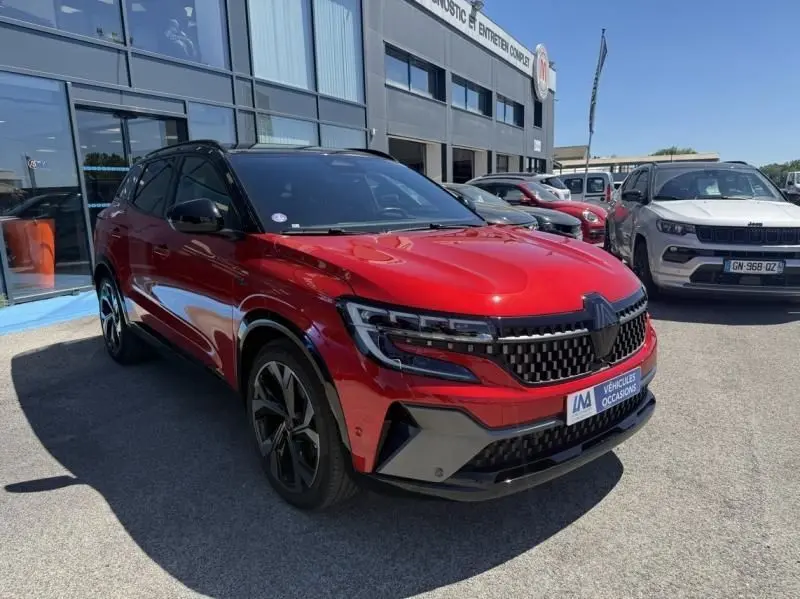 Renault Austral rouge flamme en 3/4 avant droit, avec calandre noire et jantes alliage distinctives, stationné devant un bâtiment.