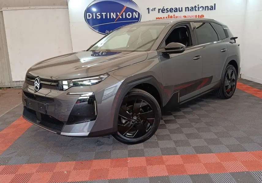 Vue 3/4 avant d'une Citroën C5 hybride gris foncé avec jantes noires et calandre moderne, en intérieur showroom.