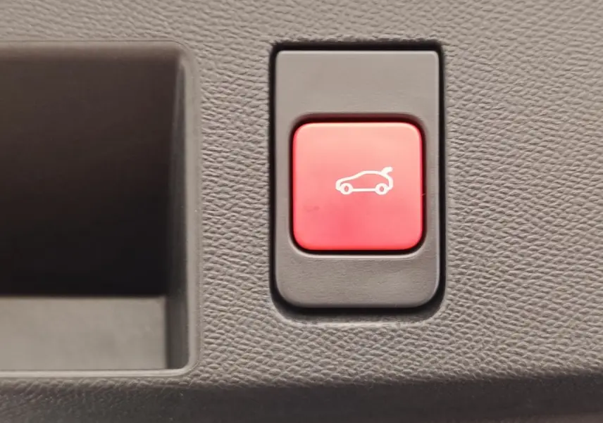 Bouton rouge d'ouverture électrique du coffre sur tableau de bord texturé gris foncé d'une Citroën C5 hybride.
