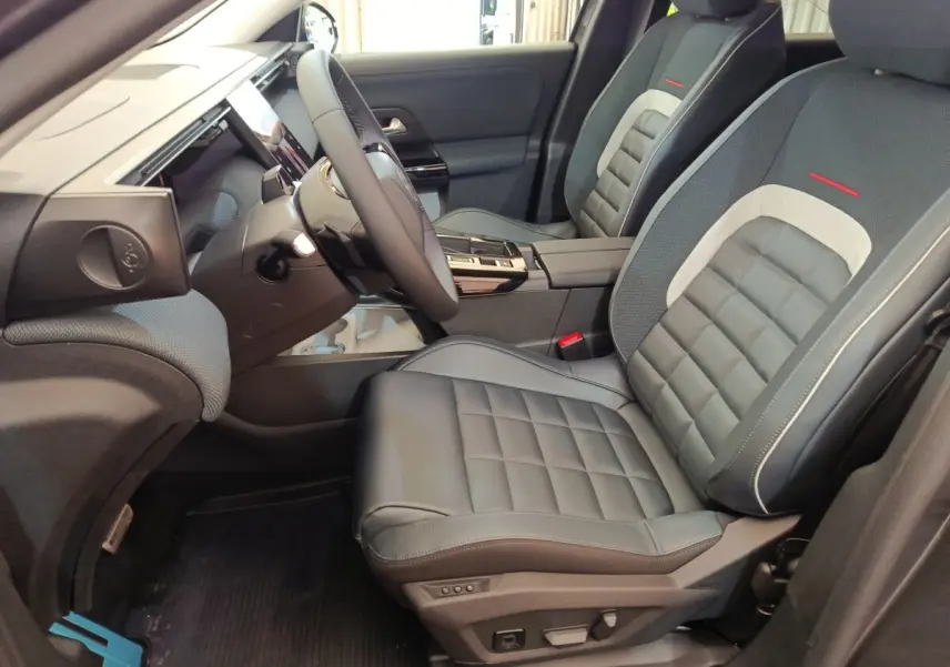 Vue intérieure côté conducteur du Citroën C5 Hybride 2025, sièges cuir gris avec surpiqûres rouges et tableau de bord moderne.