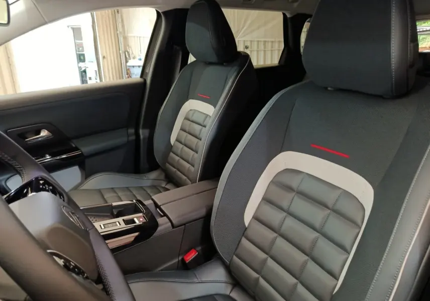 Vue intérieure rapprochée des sièges avant gris foncé avec surpiqûres et détails rouges du Citroën C5 Hybride 2025.