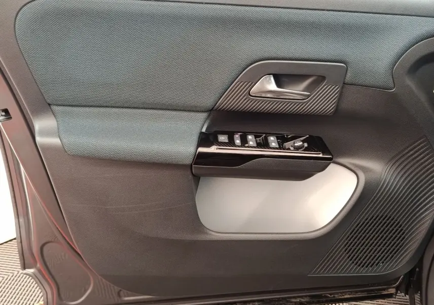 Gros plan sur la porte avant gauche intérieure de la Citroën C5 hybride gris foncé, avec commandes de vitres et poignée argentée.