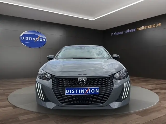 Vue frontale d'une Peugeot 208 gris foncé 2024 avec phares LED et calandre noire distinctive en showroom.