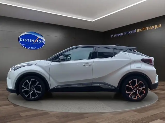 Profil côté gauche du Toyota C-HR Hybride blanc avec toit noir, roues alliage et lignes anguleuses modernes.