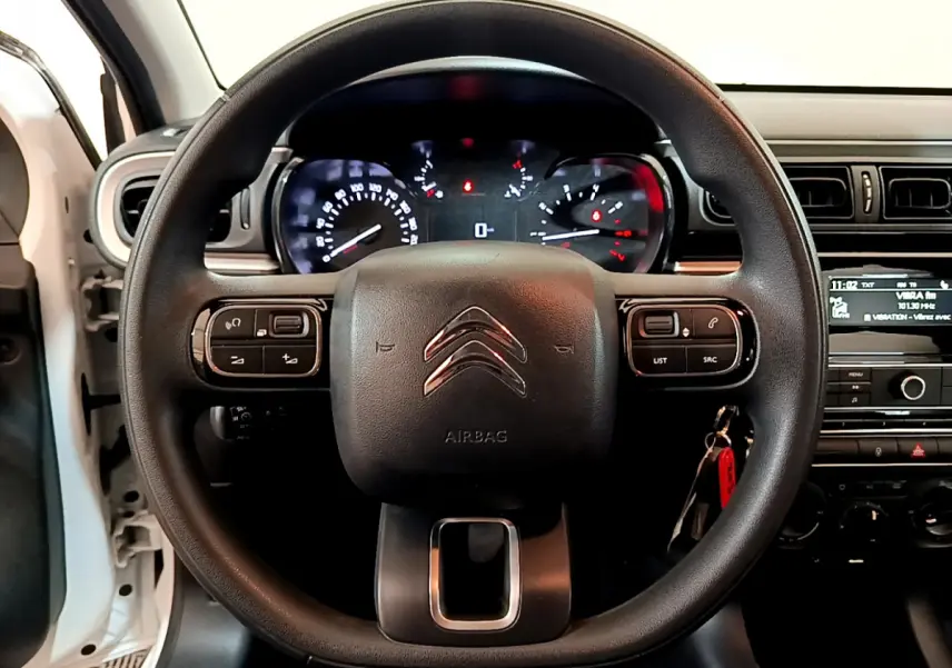 Vue frontale du volant noir de la Citroën C3 blanche 2018 avec commandes multifonctions et tableau de bord éclairé.