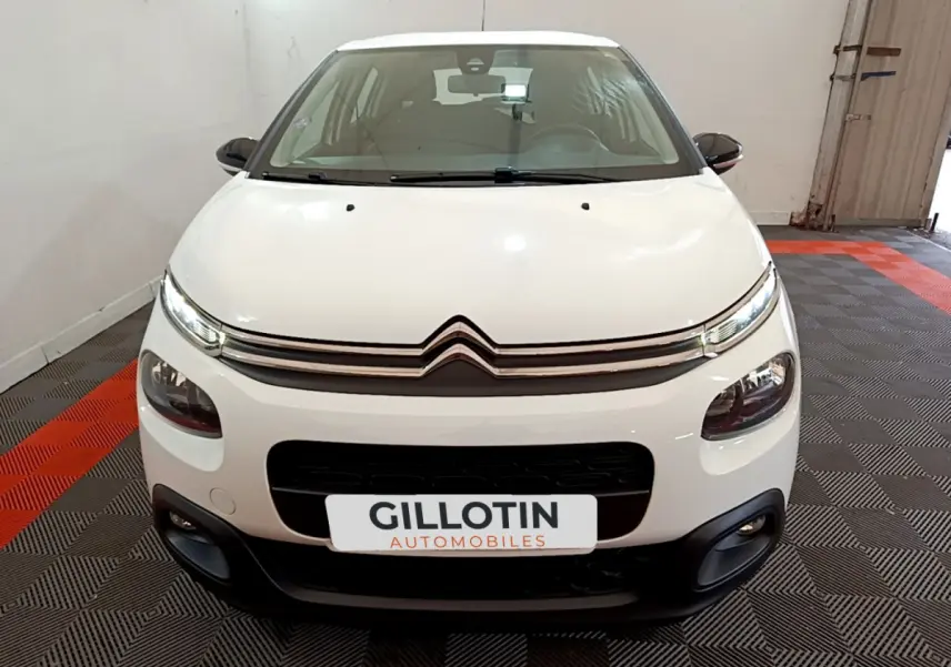 Vue frontale d'une Citroën C3 blanche de 2018 avec phares LED et calandre chromée, en intérieur showroom.