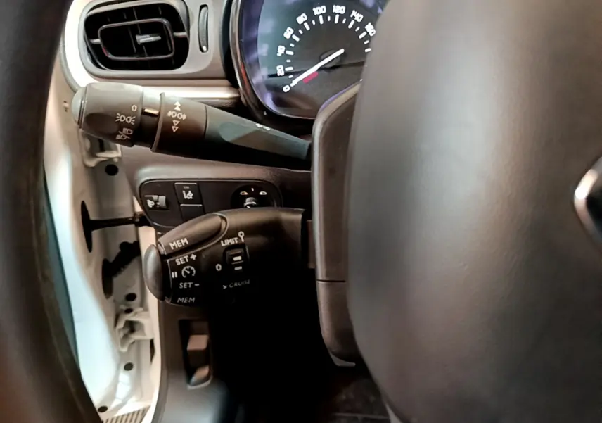 Gros plan sur le volant et les commandes de régulateur de vitesse d'une Citroën C3 blanche, côté gauche.