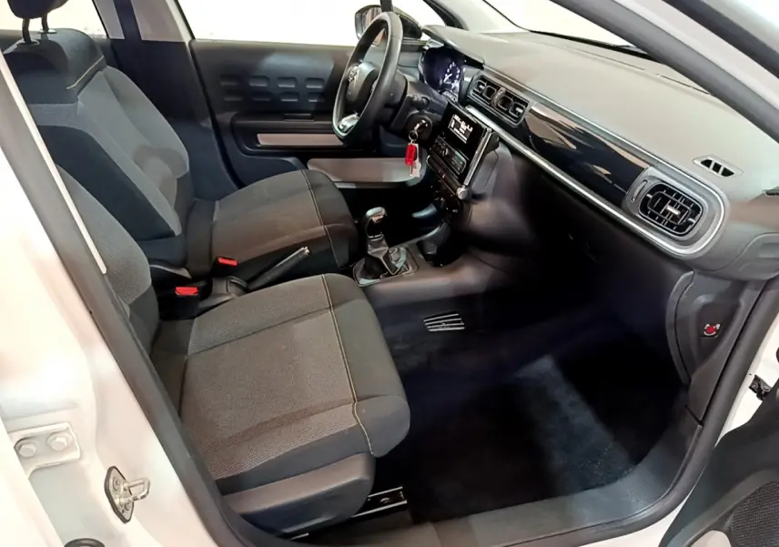 Intérieur avant droit d'une Citroën C3 blanche 2018, avec sièges tissu gris et tableau de bord noir brillant.