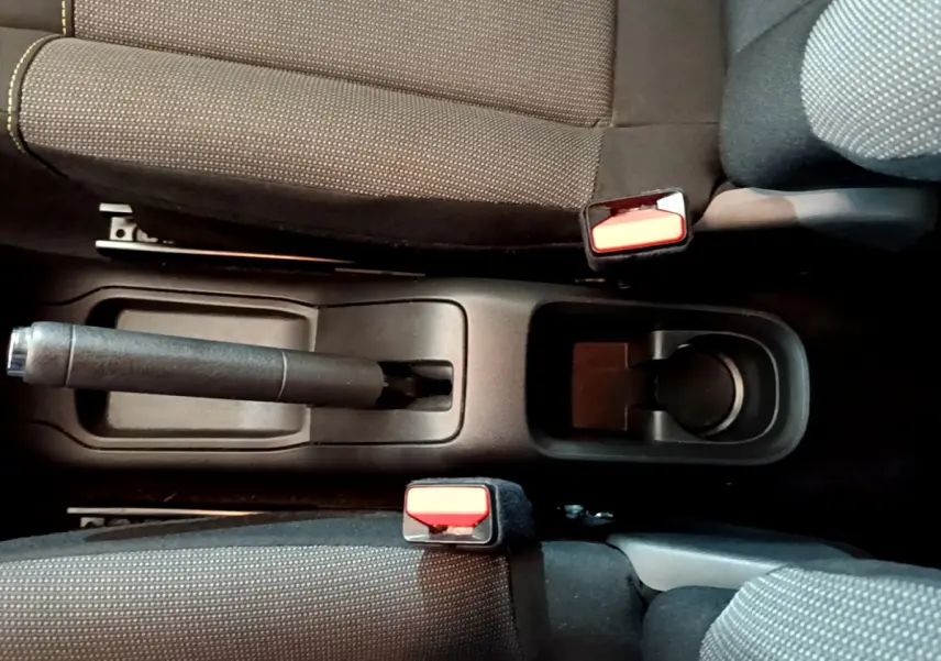Vue plongeante sur la console centrale noire d'une Citroën C3 blanche, montrant frein à main et ceintures rouges.