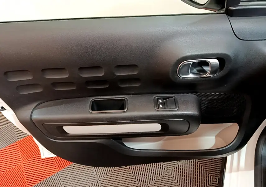 Gros plan sur la porte côté conducteur de la Citroën C3 blanche, montrant la poignée intérieure et les commandes de vitres électriques.