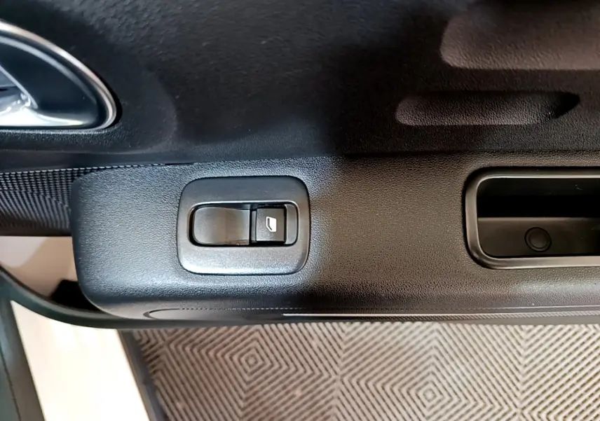 Gros plan sur la commande de lève-vitre côté conducteur de la porte intérieure noire d'une Citroën C3 blanche.