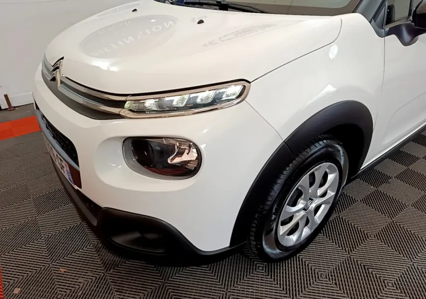 Vue 3/4 avant droit d'une Citroën C3 blanche mettant en valeur ses phares LED et ses protections noires contrastantes.