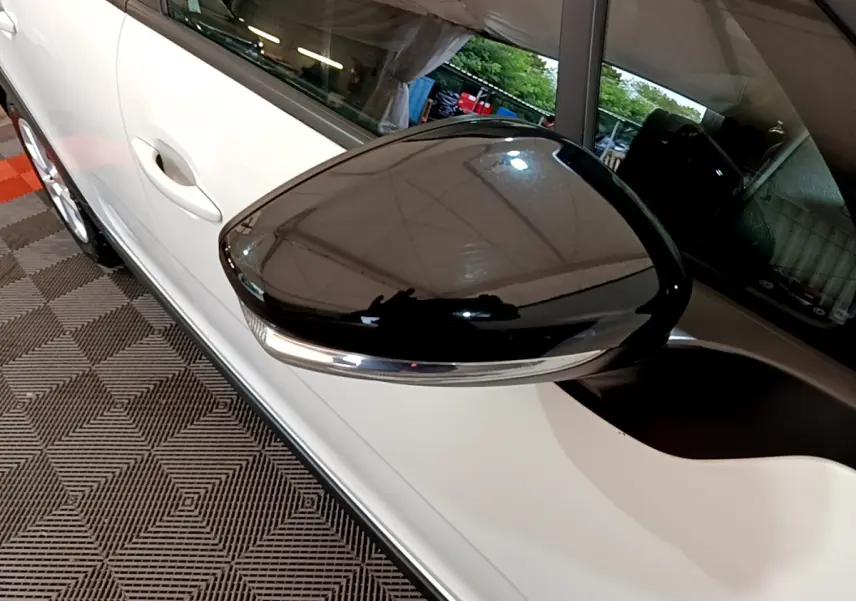 Gros plan sur le rétroviseur noir brillant côté gauche d'une Citroën C3 blanche, avec poignée de porte visible.