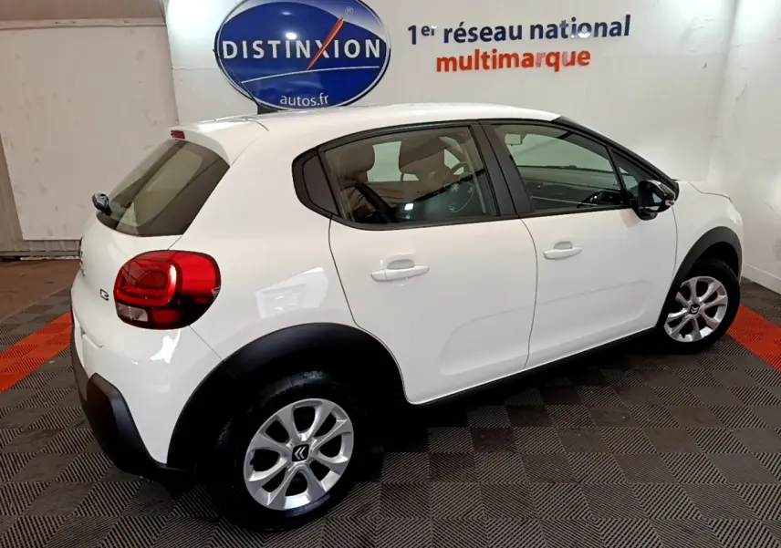 Citroën C3 blanc vue 3/4 arrière droit, avec jantes alliage et protections noires sur les passages de roues.