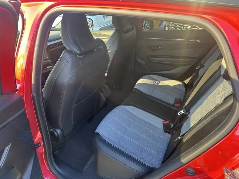 Vue intérieure arrière côté gauche de la Renault Mégane E-Tech Electric rouge flamme, montrant les sièges arrière bi-matière tissu et cuir.