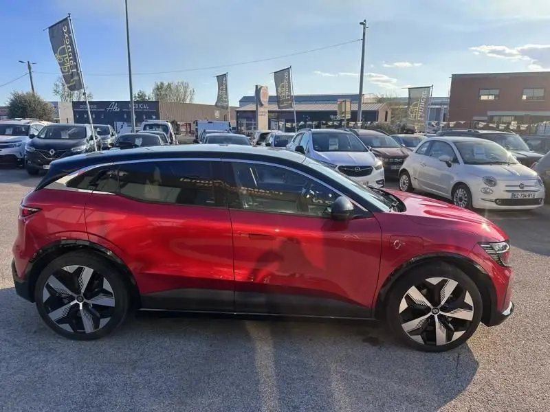 Vue de profil côté gauche d'une Renault Mégane E-Tech Electric rouge flamme 2023 avec jantes noires et grises distinctives.