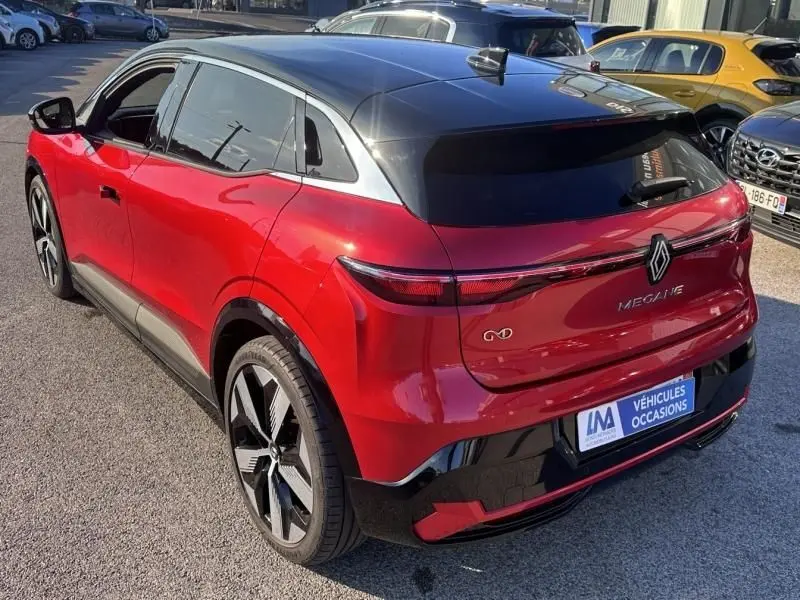 Vue 3/4 arrière droite de la Renault Mégane E-Tech Electric rouge flamme avec toit noir et feux arrière fins.