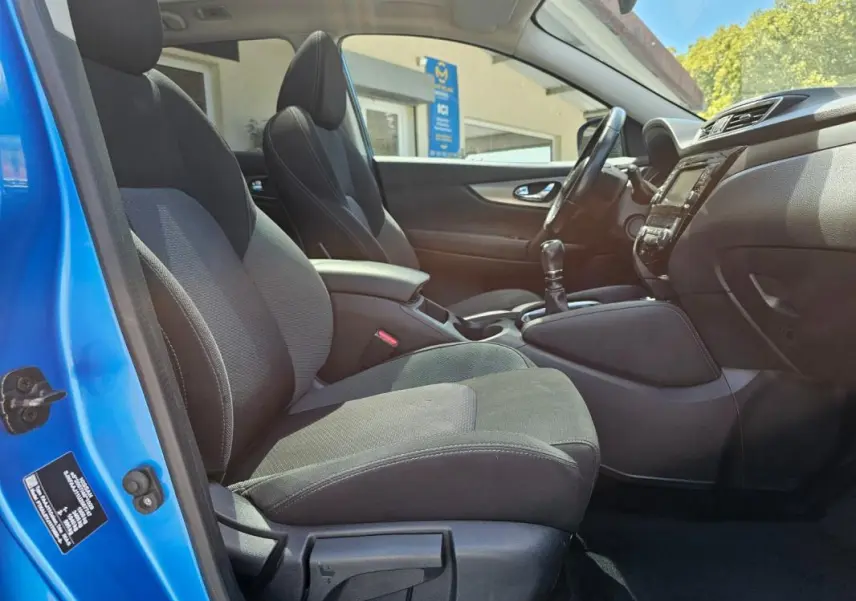 Intérieur du Nissan Qashqai bleu 2019, vue côté conducteur, sièges noirs et levier de vitesse manuel visible.