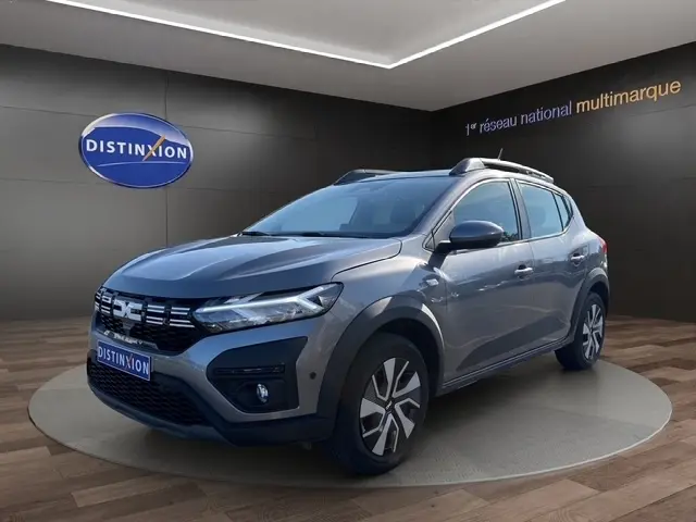 Vue 3/4 avant d'une Dacia Sandero Stepway gris foncé avec barres de toit et jantes alliage en showroom.