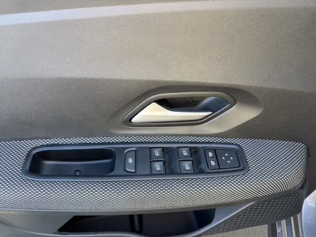 Gros plan sur la commande des vitres électriques et la poignée intérieure côté conducteur de la Dacia Sandero Stepway gris foncé 2025.