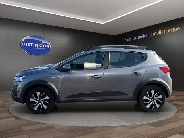 Vue latérale droite d'une Dacia Sandero Stepway gris foncé avec rails de toit et jantes distinctives en concession.
