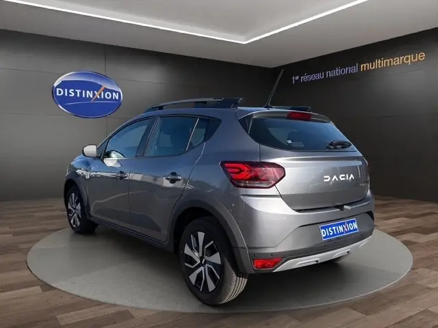 Dacia Sandero Stepway gris foncé vue 3/4 arrière droit en intérieur avec rails de toit et feux LED distinctifs.