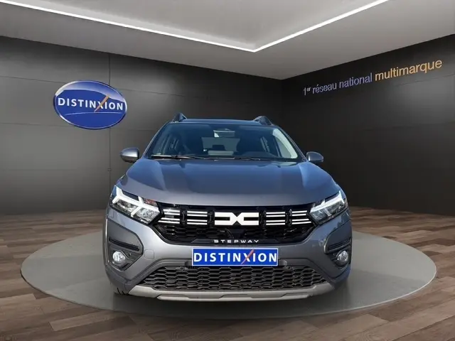 Vue frontale d'une Dacia Sandero Stepway gris foncé avec calandre noire et logo distinctif, en showroom.
