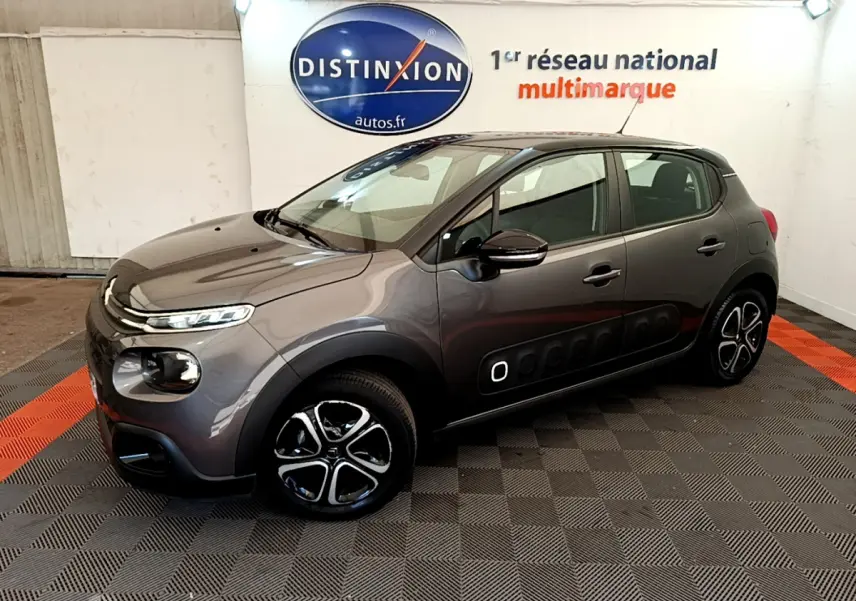 Citroën C3 gris foncé vue 3/4 avant droit, avec protections latérales noires et jantes stylisées en concession.