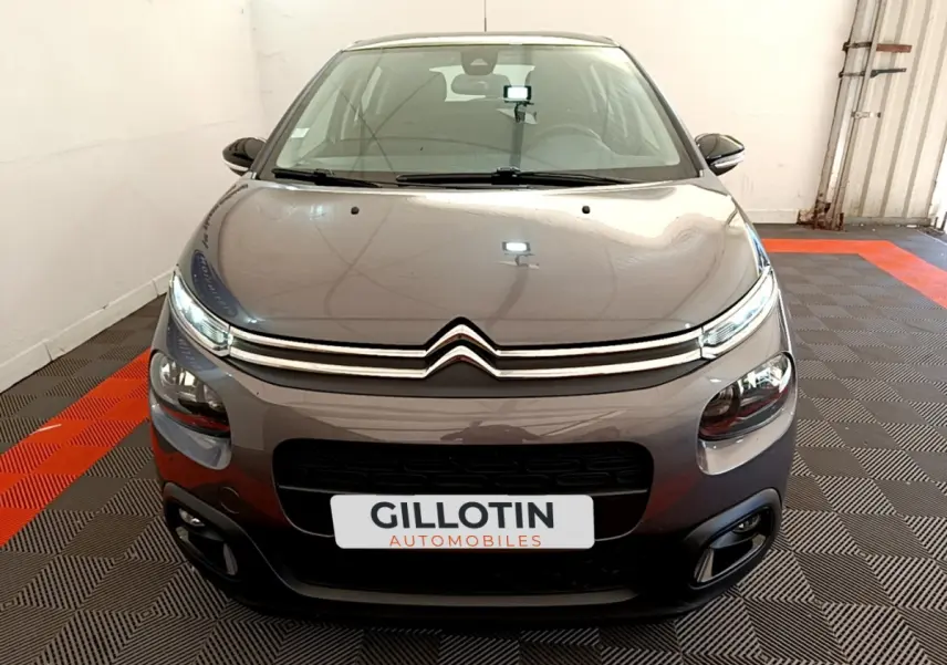 Vue frontale d'une Citroën C3 gris foncé 2019 avec phares LED et calandre chromée dans un showroom.