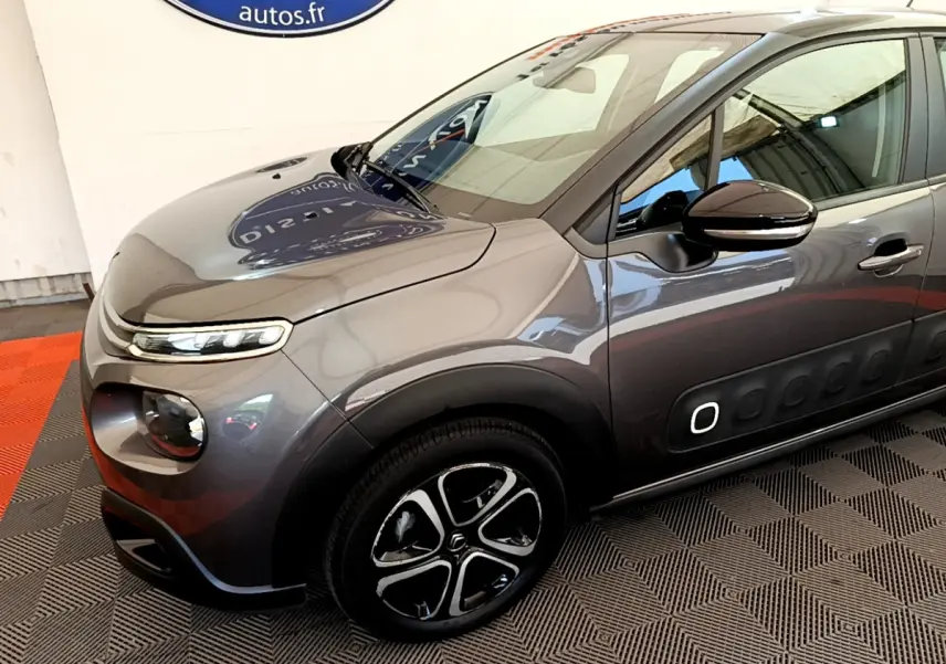 Vue 3/4 avant droit d'une Citroën C3 gris foncé avec jantes noires et détails Airbump blancs sur la porte.