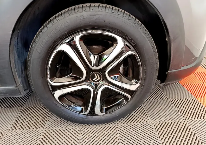 Gros plan sur la roue avant droite d'une Citroën C3 gris foncé, mettant en valeur la jante noire et chromée au design distinctif.