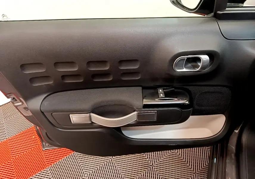Vue intérieure côté gauche de la porte avant d'une Citroën C3 gris foncé avec poignée et commandes de vitres intégrées.