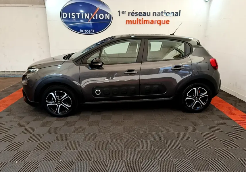 Profil côté gauche d'une Citroën C3 gris foncé 2019 avec protections latérales noires et jantes stylisées en intérieur showroom.