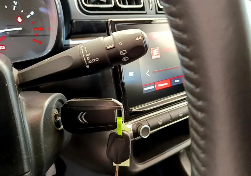 Gros plan intérieur sur la clé insérée et le commodo d'essuie-glace, avec écran tactile et volant cuir visibles.