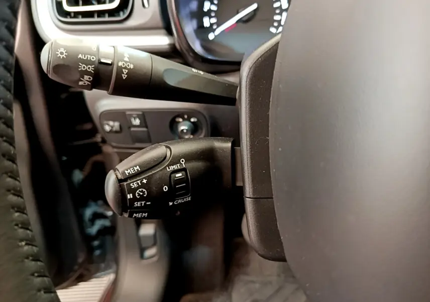 Gros plan sur la commande de régulateur de vitesse à gauche du volant cuir dans l'habitacle gris foncé d'une Citroën C3 2019.