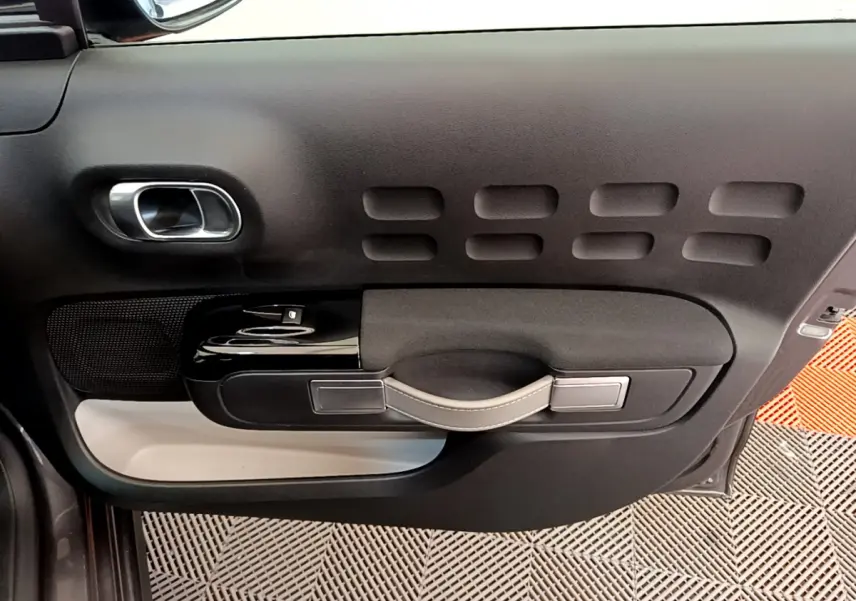 Vue intérieure côté gauche de la porte avant d'une Citroën C3 gris foncé avec poignée et commandes de vitre noires.