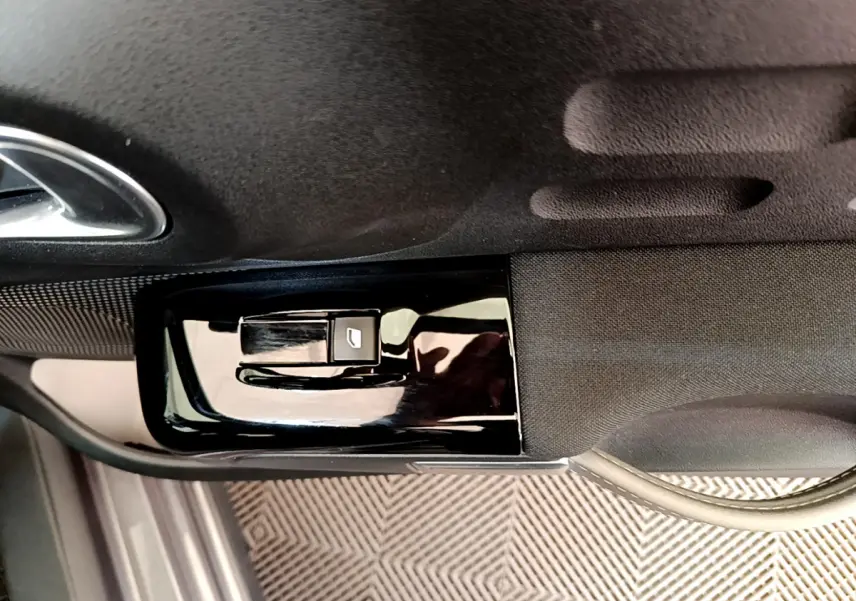 Gros plan sur le bouton de commande de vitre électrique côté conducteur dans l'habitacle d'une Citroën C3 gris foncé.