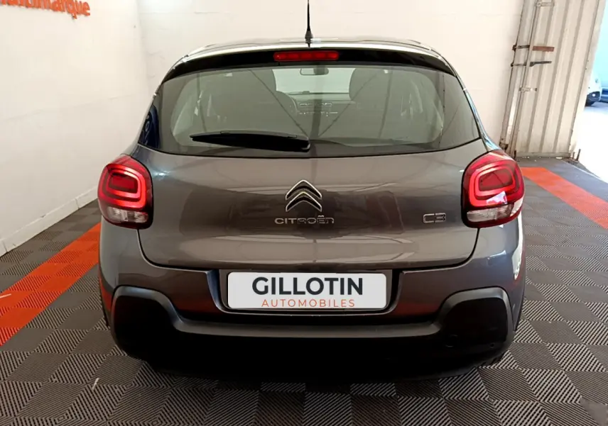 Vue arrière d'une Citroën C3 gris foncé avec feux arrière allumés dans un garage lumineux.