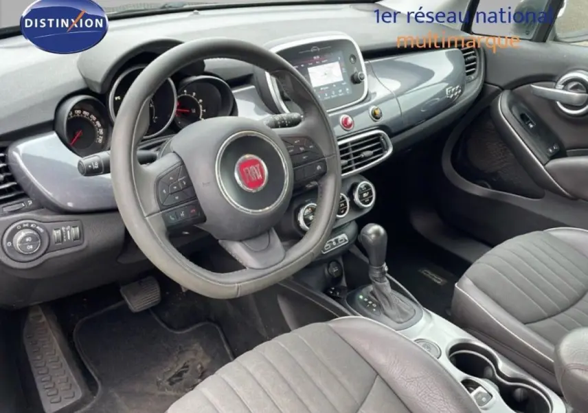 Vue intérieure côté conducteur du Fiat 500X gris foncé, montrant le volant, la console centrale et les sièges avant.