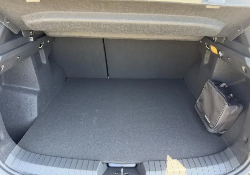 Coffre ouvert du Dacia Duster Hybrid-G 150 4X4 Journey 2026, vue intérieure avec tapis noir et trousse de secours fixée.