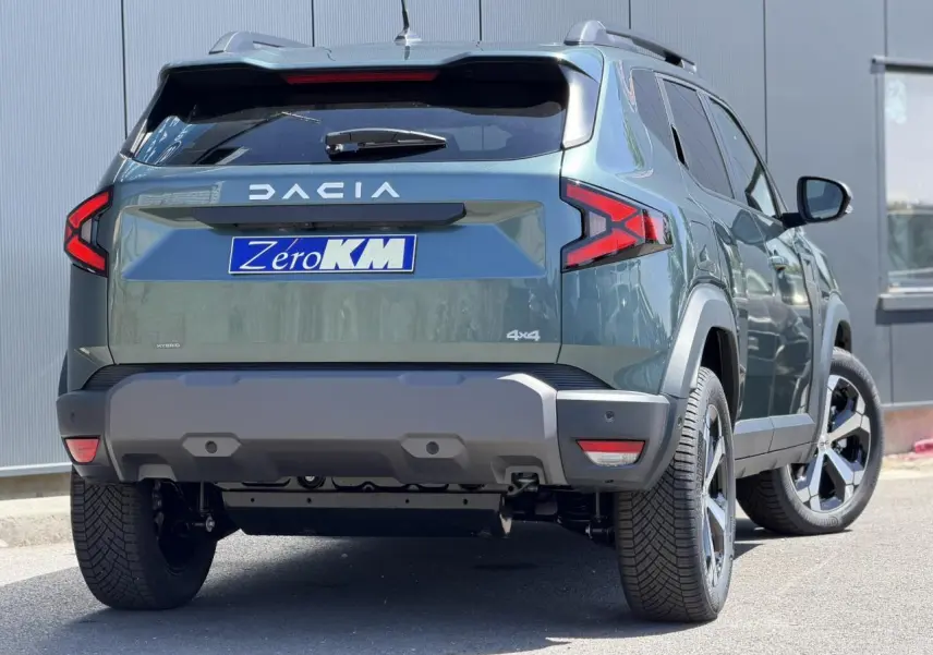 Vue 3/4 arrière droite du Dacia Duster Hybrid-G 150 4x4 en Vert Cèdre avec jantes alliage et barres de toit noires.